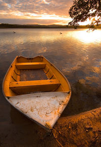 Boat moored on beach against sky during sunset