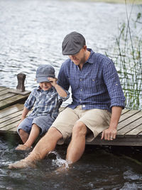 Man with son sitting on jetty at lake