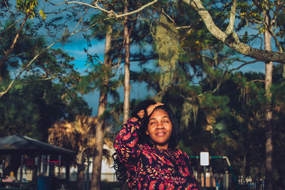 Portrait of smiling young woman standing against trees