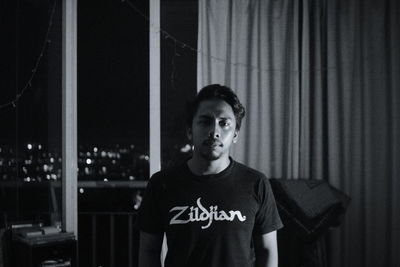 Portrait of young man standing against curtain at home