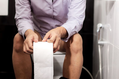 Midsection of man holding toilet paper while sitting on bowl 