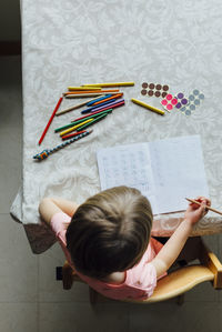 Top view of anonymous little girl doing homework besides a window