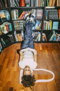 High angle view of woman reading book while lying down with feet up on shelf in bookstore