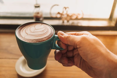 Blue cup of coffee with full latte art on wooden table.