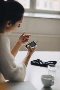 Close-up of woman checking blood sugar level in glaucometer while sitting at table