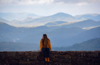 Woman sitting on retaining wall against sky