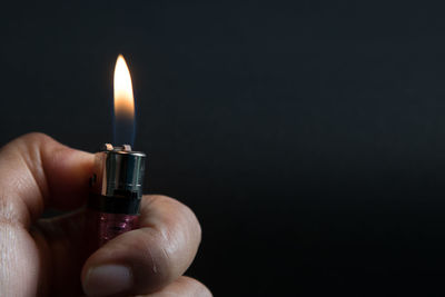Close-up of hand holding lit cigarette lighter against black background