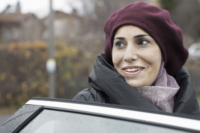 Smiling woman looking away by car door outdoors