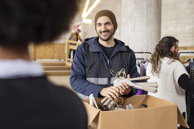 Smiling male worker unpacking hangers from cardboard box at recycling center