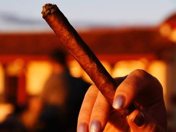 Close-up of hand holding cigarette against sky