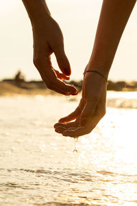 Close-up of hand on sea shore during sunset