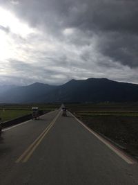 Vehicles on road amidst field against sky