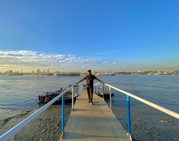 Rear view of man standing on pier at sea against blue sky