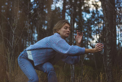 Young woman with short hair dancing against trees in forest