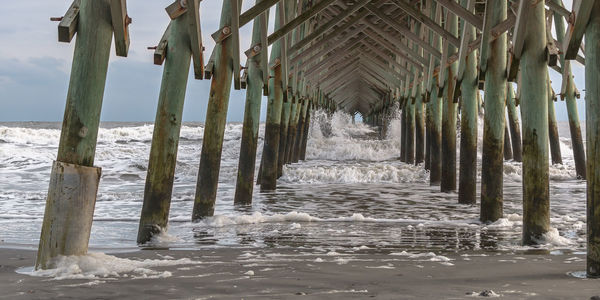 Full frame view looking out to sea under a wooden pier with waves crashing