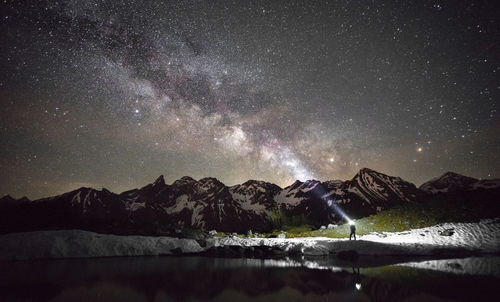 Distant view of man with flashlight standing by bavarian alps against star field at night