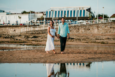 Full length of couple standing on beach against sky