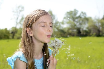 Girl blowing dandelion seeds on field