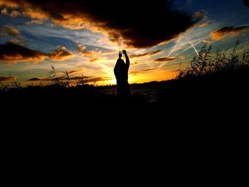 Silhouette man standing on field against sky during sunset