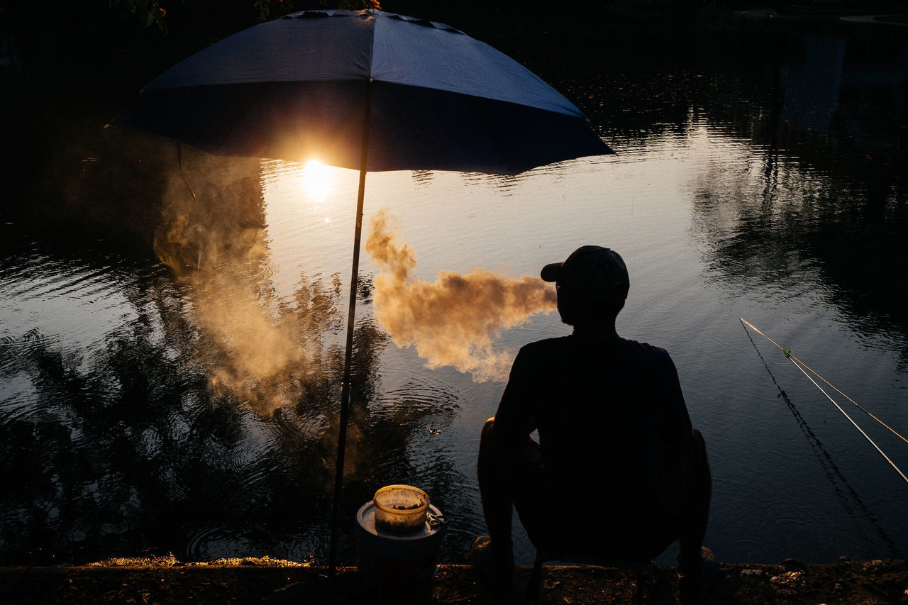 real people, water, rear view, one person, lifestyles, umbrella, leisure activity, sitting, nature, men, sky, lake, sunset, silhouette, beauty in nature, adult, standing, outdoors, rain, looking at view