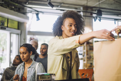 Young man taking shopping bag while female customer waiting in line at store