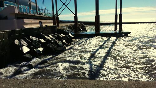 Surface level of railing by sea against sky on sunny day