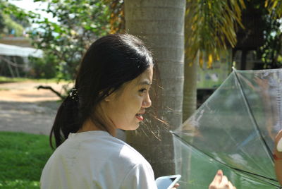 Close-up of woman holding umbrella by tree trunk