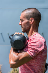 Side view male athlete with strong body doing exercises with heavy metal kettlebell during intense workout in summer