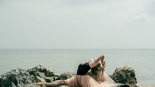 Full length of woman exercising on rock at beach against sky