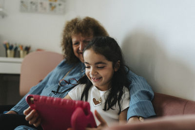 Smiling girl using digital tablet with grandmother at home