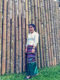 Portrait of smiling girl in traditional clothing standing by bamboos wall