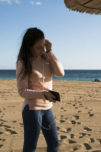 Caucasian woman listening to music with headphones on the beach with the sea in the background