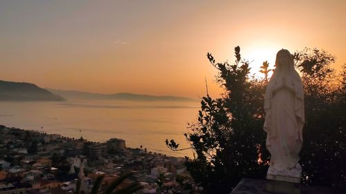 Woman standing by sea against sky during sunset