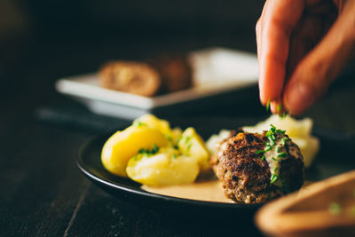 Cropped hand putting chopped chives on meatball