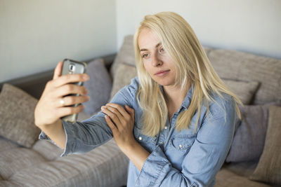 Young woman taking selfie through phone while sitting on sofa at home