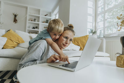 Boy doing mischief on laptop while standing behind mother at home