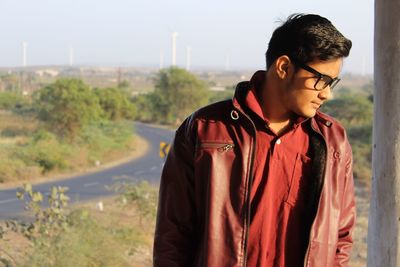 Young man standing by road against sky