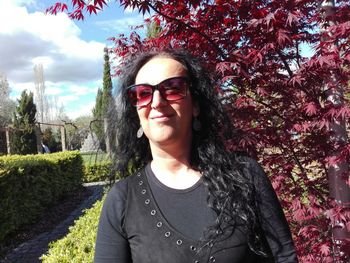 Smiling woman wearing sunglasses against plants at park