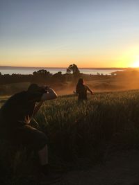 Ma photographing while standing by plants against sky during sunset