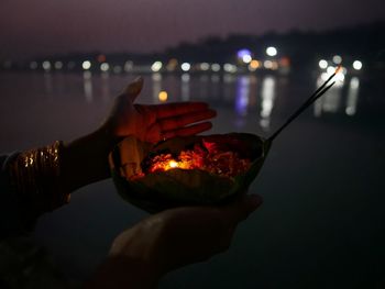 Cropped hands holding religious equipment by ganges river at night