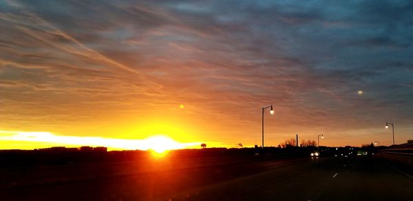 Cars on road against dramatic sky during sunset