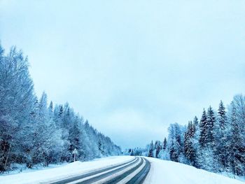 Road by snow covered landscape against sky