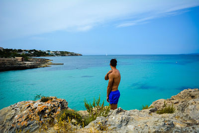 Side view of shirtless man standing on cliff against sea