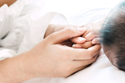 Cute baby boy holding person finger while lying on bed