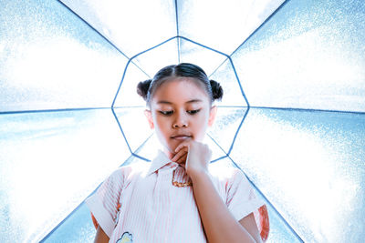 Low angle view of thoughtful girl standing against ceiling