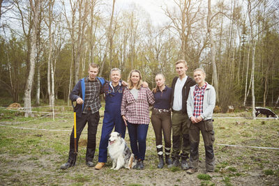 Full length of farmer with family standing on field against trees