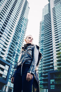 Portrait of young woman standing against modern buildings in city