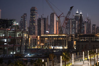 Illuminated buildings and cranes in city at night