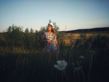 Man standing amidst grass on field against clear sky