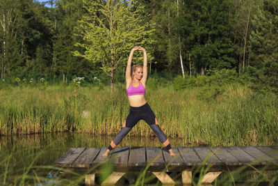 Full length of woman with pink arms raised against trees